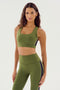 A woman is wearing the Lexi Rigor Bra in olive and black from SPLITS59, paired with matching high-waisted leggings featuring black and white side stripes. The ensemble is crafted from a blend of nylon and spandex, and she stands against a plain white background.