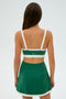 A woman is shown from the back, wearing an SPLITS59 Monah Rigor Bra in Arugula/White with a green skirt, ready for her gym workouts.
