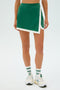 A person wearing the Monah Rigor Skort in Arugula/White from SPLITS59, paired with white socks and sneakers featuring green accents, stands against a plain background.