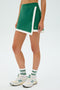 A person stands against a plain background wearing SPLITS59's Monah Rigor Skort in Arugula/White and white sneakers.