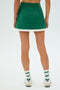 A person is seen from the back wearing a SPLITS59 Monah Rigor Skort in Arugula/White, along with white socks with green stripes and white sneakers.