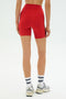 A person stands with their back to the camera, wearing SPLITS59’s Ella High Waist Airweight Short in Pirate Red/Indigo, paired with white socks and sneakers, set against a plain background.