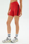 A person wearing SPLITS59 Ella High Waist Airweight Shorts in Pirate Red/Indigo, white SPLITS59 socks, and gray sneakers stands on a white background.