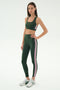 A woman wears the SPLITS59 Lexi Rigor Bra in Military/Blush—dark green with blush side stripes—paired with matching leggings and silver athletic shoes, standing against a plain white background.