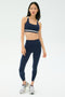 A woman stands against a plain background wearing the SPLITS59 Miles High Waist Rigor 7/8 leggings in Indigo/White with matching sports bra and silver athletic sneakers.
