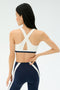 A person wearing the SPLITS59 Miles Rigor Bra in Indigo/White with crisscross straps and navy leggings stands facing away, hand resting on their back.