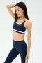 A woman wears the SPLITS59 Miles Rigor Bra in Indigo/White, standing against a plain light background with one arm raised and eyes closed.