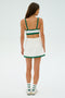 Facing away, a woman wears the SPLITS59 Monah Rigor Bra in white with green trim as part of a matching crop top and skirt set, paired with white socks and sneakers.