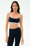 A woman stands against a plain background wearing the SPLITS59 Emerson Airweight Bra in Indigo/Dove Grey, paired with matching high-waisted leggings—ideal for Pilates or hot yoga.