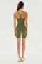 A person stands facing away, wearing the SPLITS59 Airweight 6” Short Jumpsuit in olive, complemented by beige sneakers.
