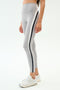Person wears SPLITS59 Emerson Airweight High Waist leggings in Dove Grey/Indigo—light gray with white and black side stripes—for a sculpted look, paired with white athletic shoes, standing against a plain background.