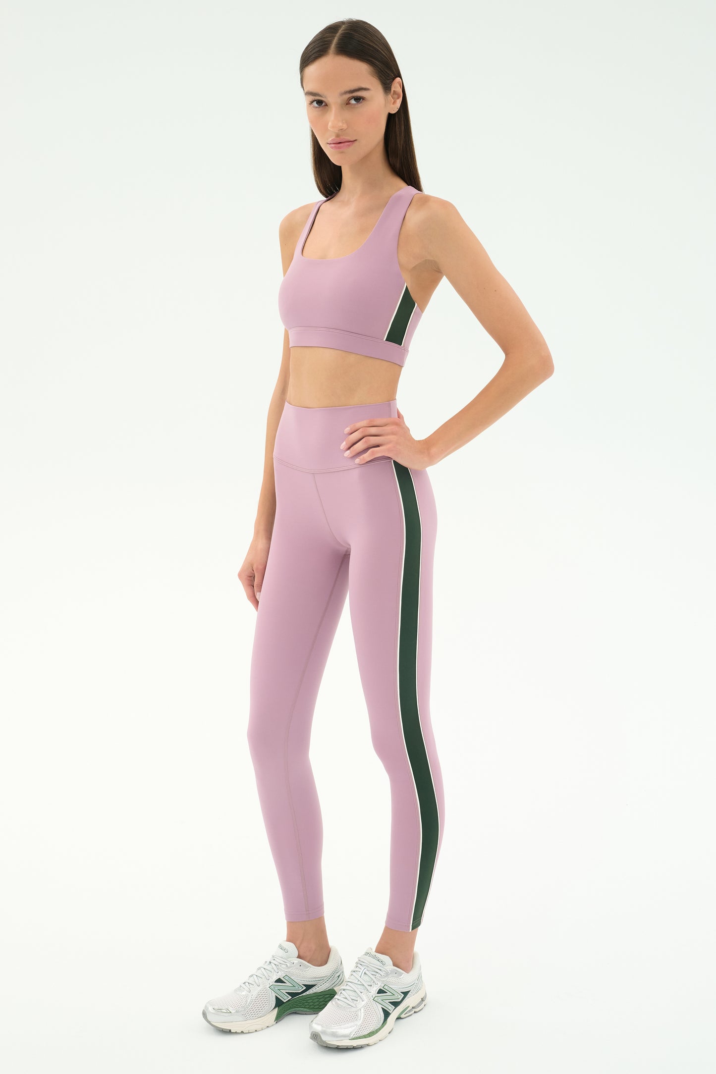 A woman wears the SPLITS59 Lexi Rigor Bra in Blush/Military with matching leggings and white sneakers, standing against a plain white background.