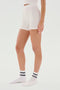 Person standing in white seamless fitted SPLITS59 Theo Rib Short - White and white socks with black and white logo. Cropped at chest level, side view against a plain white background, showcasing the tailored comfort of the SPLITS59 Theo Rib Short - White's classic design.