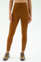 A person stands against a plain background wearing SPLITS59 Amber Airweight High Waist 7/8 leggings in Honey/Indigo with black side stripes, paired with brown sneakers.