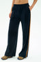 A person wears the SPLITS59 Luca Airweight Trouser with Stripe in Indigo/Honey, styled with colorful sneakers and a bare midriff, standing with one hand in their pocket against a plain background.