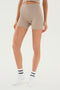 A person wearing beige Theo Rib Short - Latte high-waisted athletic shorts from SPLITS59 and white socks stands against a plain background, showcasing a blend of tailored comfort and classic design.