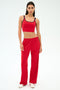 A woman stands against a plain background wearing a red crop top, SPLITS59 Maxie Rigor Track Pant in Pirate Red/Indigo, and white sneakers.