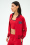 A woman in the SPLITS59 Hayes Varsity Rigor Jacket in Pirate Red, crafted from smooth nylon spandex fabric.