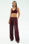 A woman stands against a white background wearing the SPLITS59 Airweight Scoop Back Bra in Dark Cherry, paired with wide-leg pants and sneakers, all made from soft nylon spandex for comfort and ease of movement.