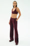 A person stands in a studio wearing the SPLITS59 Airweight Scoop Back Bra in Dark Cherry, paired with matching track pants made from soft nylon spandex and athletic shoes.