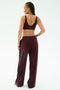 A woman faces away wearing the SPLITS59 Airweight Scoop Back Bra in Dark Cherry with matching track pants featuring black side stripes, made from soft nylon spandex, against a white background.