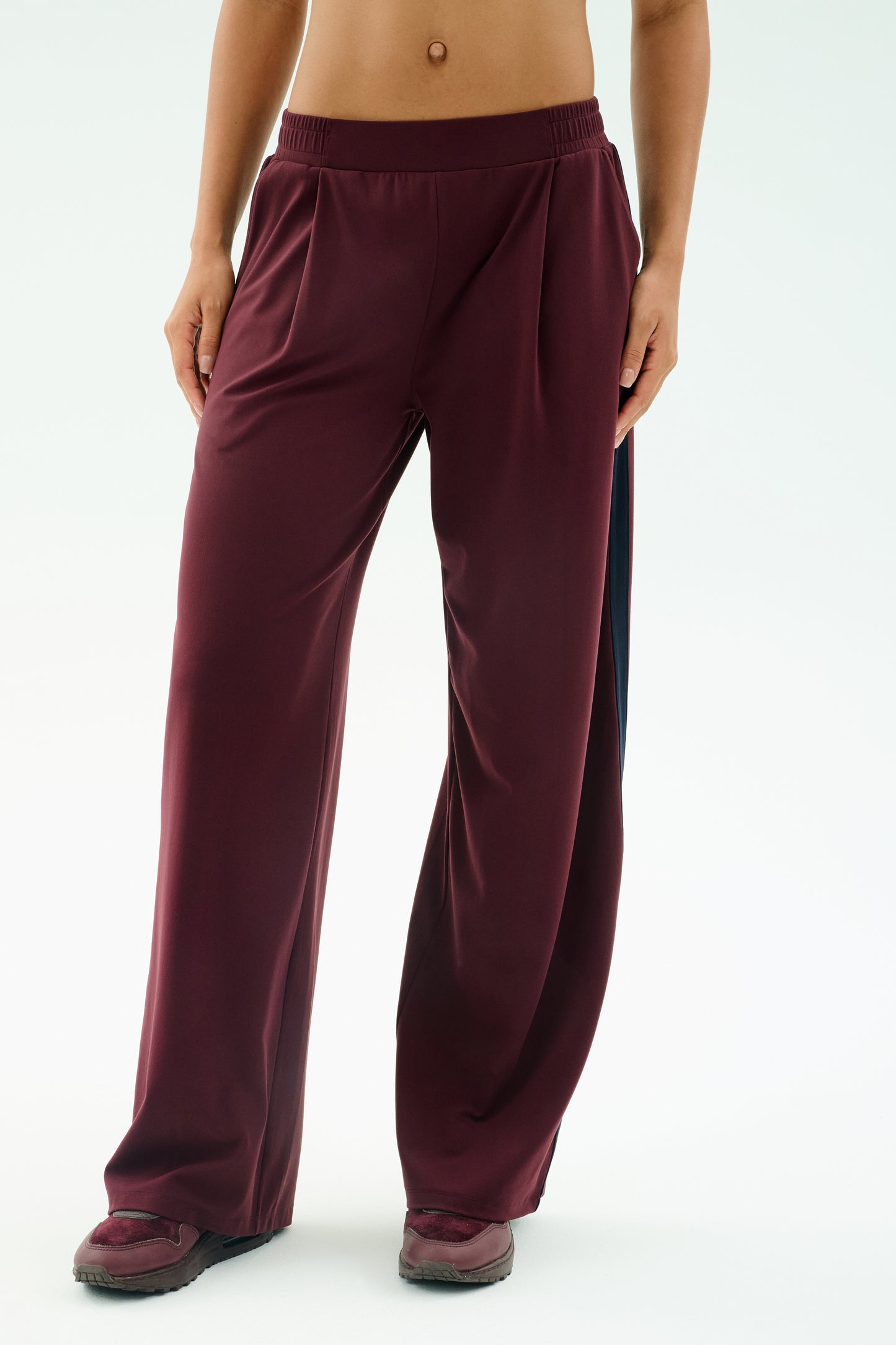 A person wearing SPLITS59's Luca Airweight Trouser with Stripe in Dark Cherry/Indigo, styled with matching maroon sneakers, shown from waist to feet against a plain background.