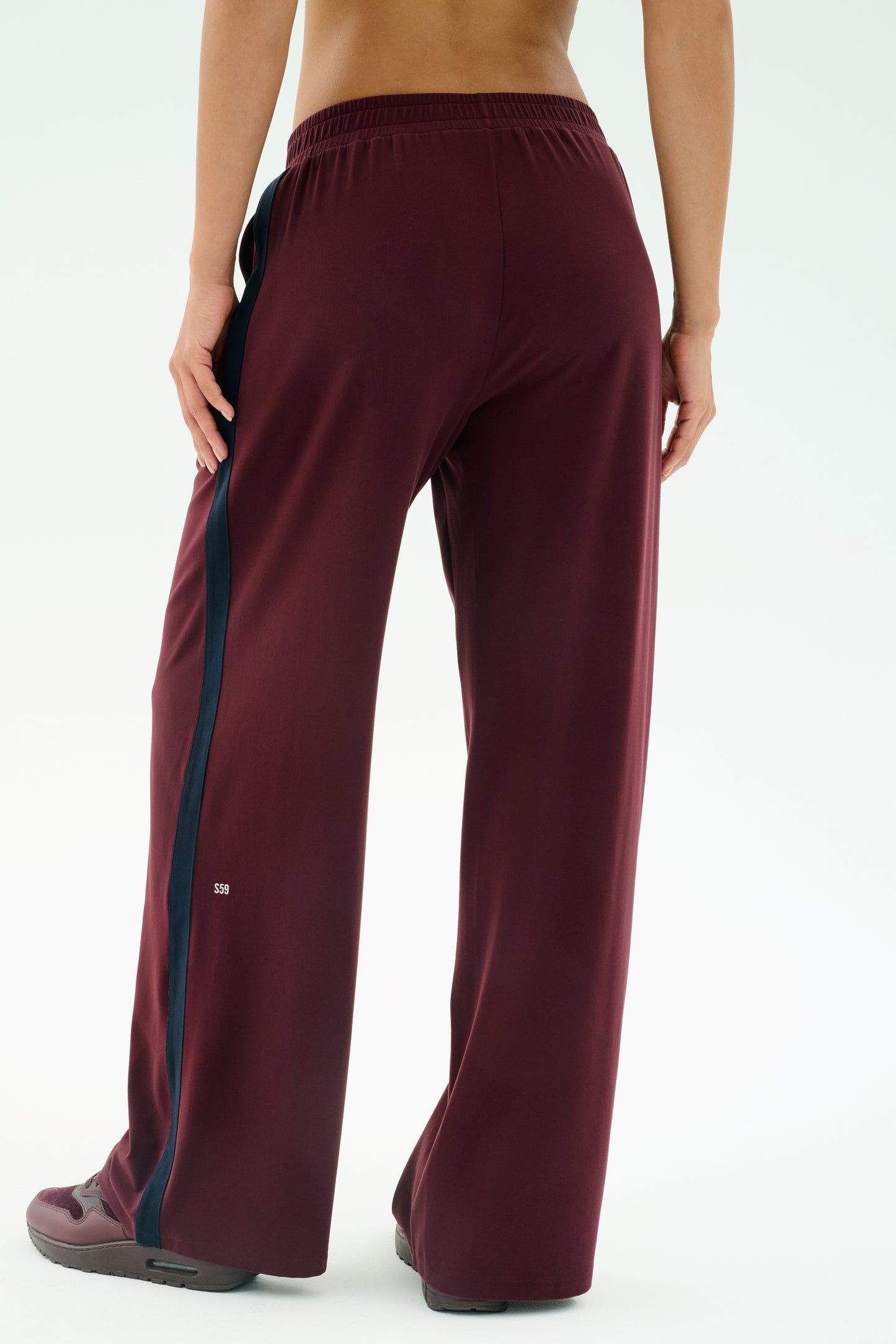 A person stands with their back to the camera, wearing SPLITS59's Luca Airweight Trouser with Stripe in Dark Cherry/Indigo, crafted from a comfy nylon-spandex blend, paired with matching shoes.