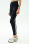 A person wearing SPLITS59’s Easton Rigor High Waist 7/8 leggings in Black/Grass, featuring compressive fabric for workout support, paired with white Nike sneakers, stands against a plain background.