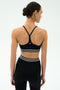 A woman with dark hair in a bun is seen from behind wearing the SPLITS59 Cali Active Rib Bra in black, paired with high-waisted, white-striped leggings against a plain light background.
