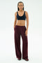 A person stands against a plain background wearing the SPLITS59 Airweight Scoop Back Bra in Indigo, loose maroon pants, and sneakers, with hands in pockets and a neutral expression.