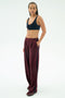 A person stands against a plain background wearing the SPLITS59 Airweight Scoop Back Bra in Indigo and loose maroon nylon track pants with hands in pockets.
