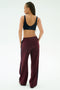 A woman faces away, wearing the SPLITS59 Airweight Scoop Back Bra in Indigo and loose maroon track pants with a dark side stripe, crafted from a soft nylon spandex blend, against a plain white background.