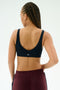 A person with braided hair is shown from the back, wearing the SPLITS59 Airweight Scoop Back Bra in Indigo, made from a soft 81% nylon and 19% spandex blend, against a plain white background.