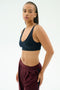 A woman wears the SPLITS59 Airweight Scoop Back Bra in Indigo, standing against a plain light background and looking at the camera.