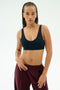 A woman with braided hair wears the SPLITS59 Airweight Scoop Back Bra in Indigo, standing against a plain light background.