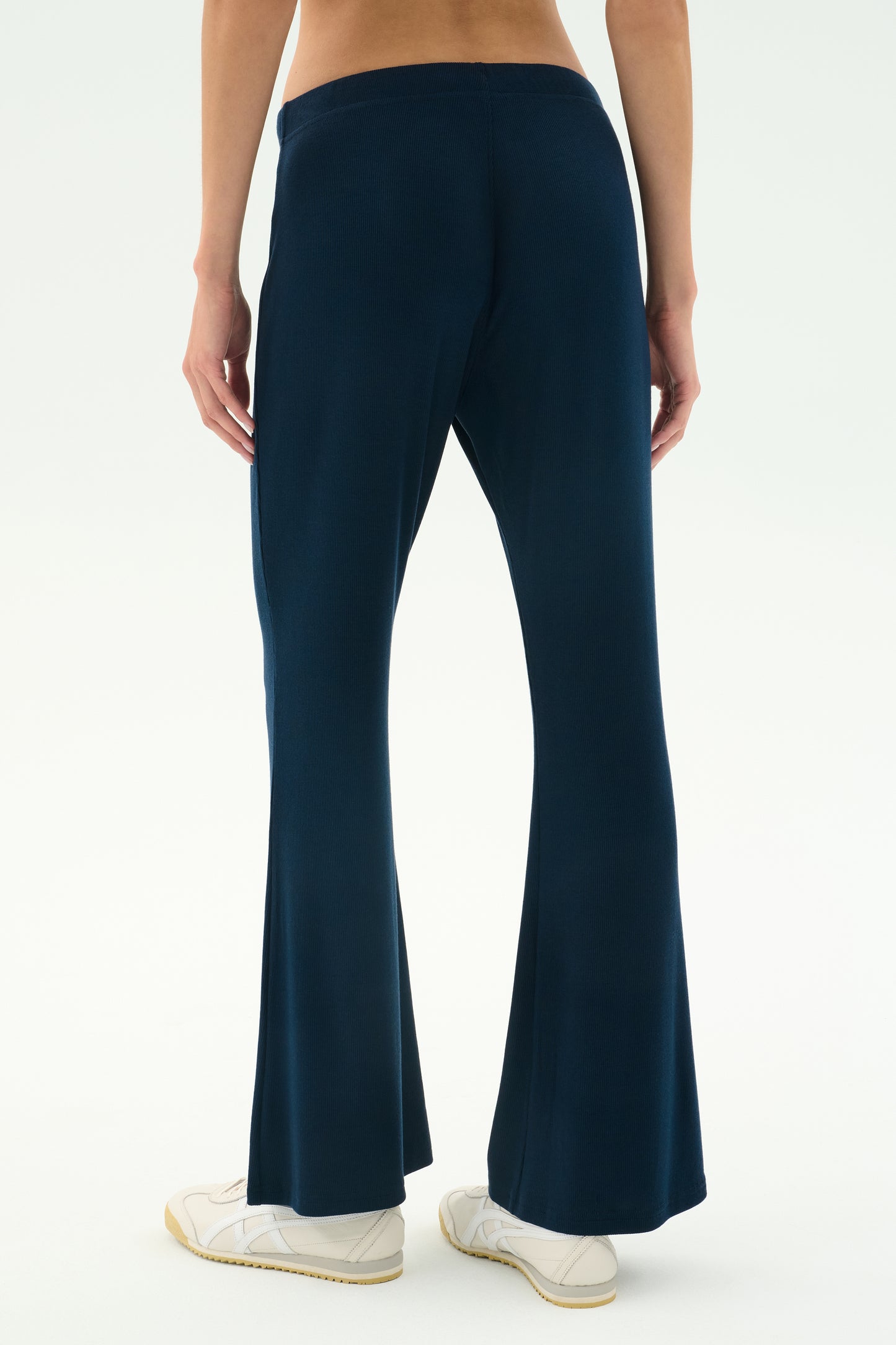 Person wears SPLITS59's Blaire Rib Pant in Indigo—dark blue, flared, soft modal fabric—paired with white sneakers. Shown waist down against a plain light background.