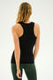 A person with long blonde hair is shown from the back, wearing a Kiki Rib Tank Full Length in Black by SPLITS59 and green leggings, standing against a plain light background, ready for some invigorating yoga.