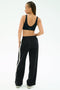 A person is seen from behind against a white background wearing the SPLITS59 Airweight Scoop Back Bra in black and wide-leg pants with a white side stripe.