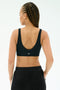 A woman with braided hair is shown from the back, wearing the SPLITS59 Airweight Scoop Back Bra in black and matching black pants against a plain white background.
