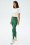 A woman stands against a plain background wearing the SPLITS59 Djuna Crop Ringer in White/Arugula, green elastane leggings with a dark side stripe, and white sneakers.