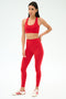 A woman poses against a plain background in SPLITS59's Airweight High Waist Legging in Pirate Red with a matching sports bra and white sneakers with red stripes—ideal attire for hot yoga.