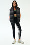 A woman faces forward wearing the SPLITS59 Summit Nylon Puffer Vest in black over a black sports bra, black leggings with a white stripe, and white sneakers—ideal for cool weather workouts against a plain background.