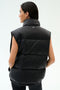 A person with long dark hair is seen from behind wearing the SPLITS59 Summit Nylon Puffer Vest in black, featuring lightweight insulation and a high collar, against a plain light background.