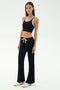 A woman stands against a plain background wearing SPLITS59’s Blaire Rib Pant in black, paired with a black crop top with white trim and white sneakers.