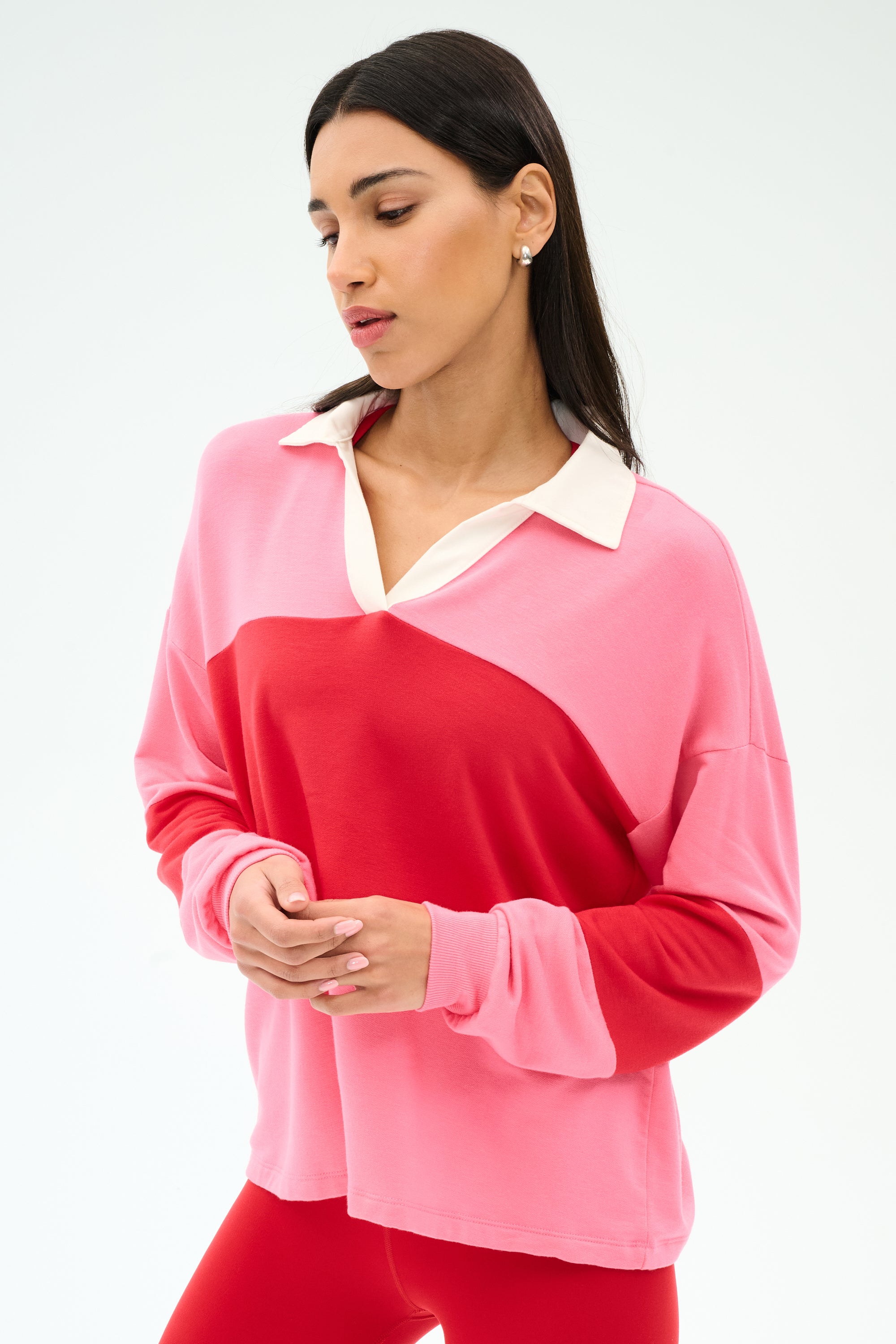 A woman stands against a plain white background wearing the SPLITS59 Katie Fleece Rugby in Strawberry/Pirate Red, a pink and red color-blocked long-sleeve top with a white collar.