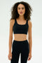 A woman with curly hair wears the SPLITS59 Airweight Rib Bra in black, paired with matching high-waisted leggings, against a plain light background.
