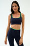 A woman faces forward wearing the SPLITS59 Cait Rigor Bra in Indigo/Grass, a supportive sports bra crafted from Rigor fabric, against a plain light background.