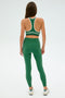 Someone in SPLITS59's green Layla Airweight High Waist 7/8 leggings and sports bra stands with their back to the camera.