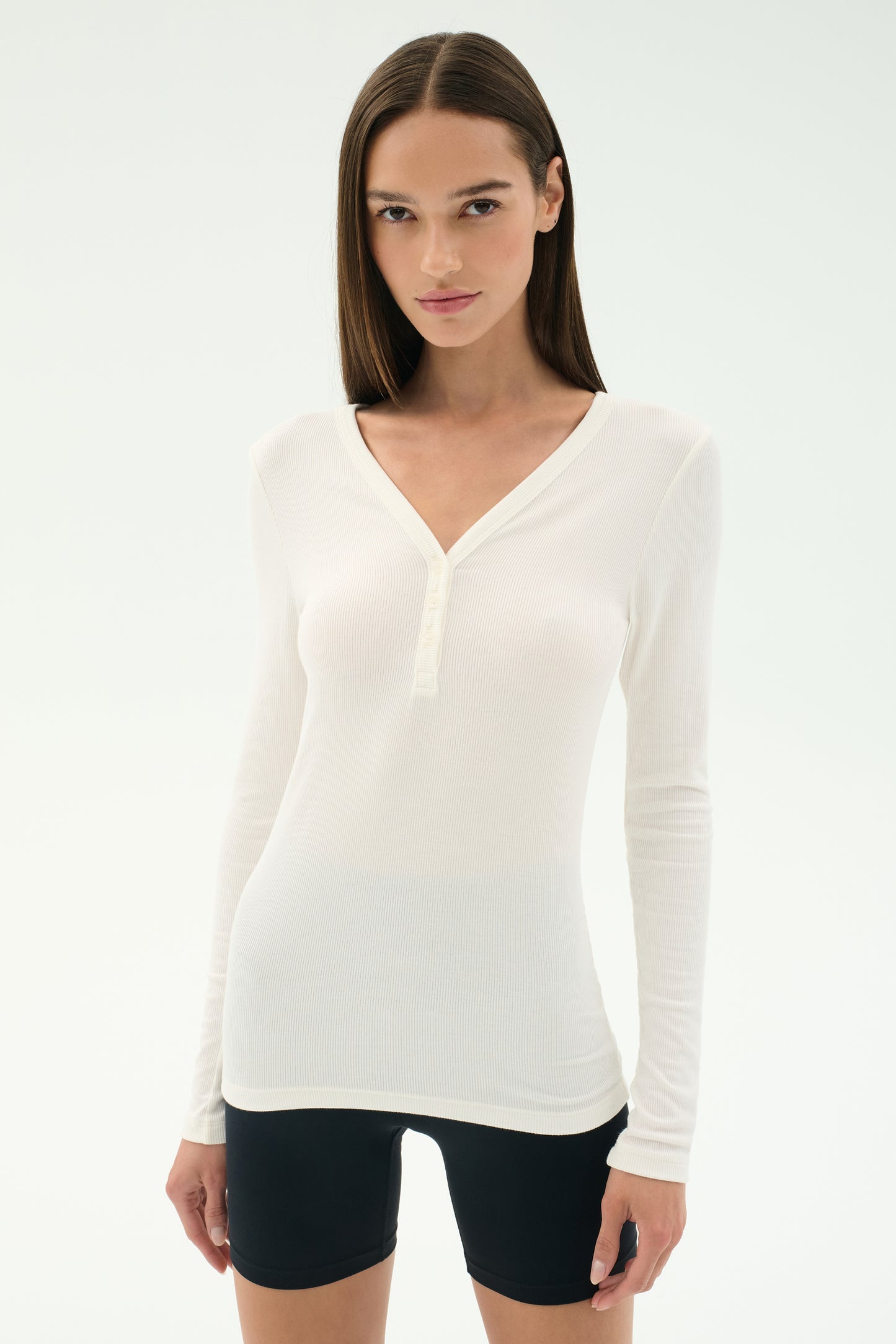 A woman wears the SPLITS59 Louise Rib Henley in white and black spandex shorts, standing against a plain white background.