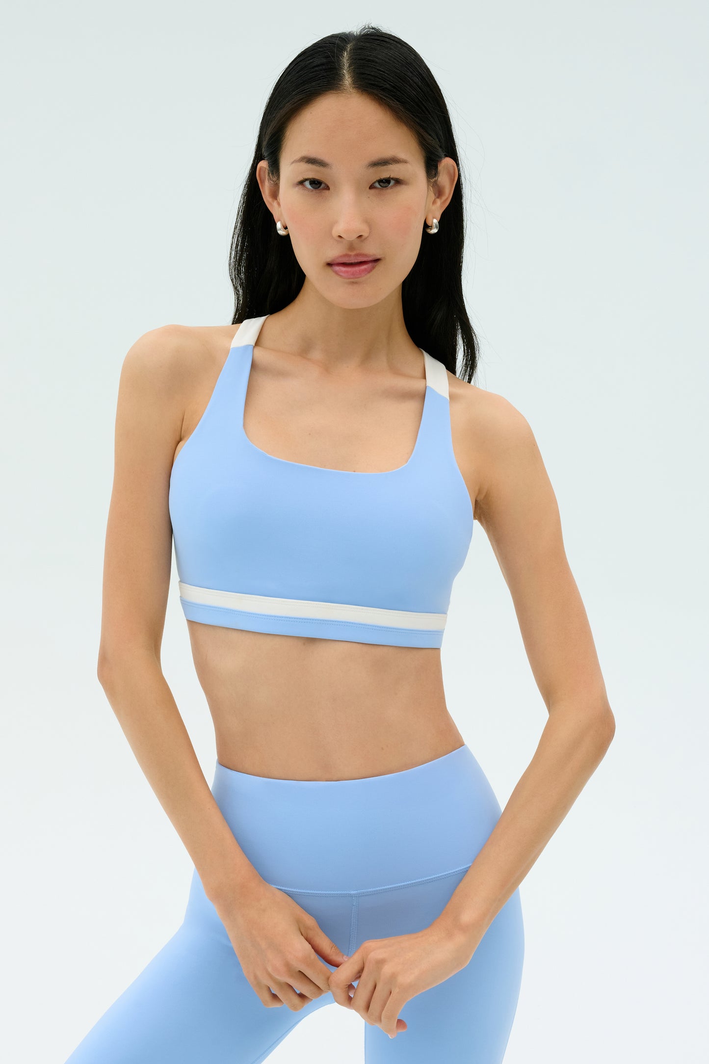 Woman with long dark hair wears the SPLITS59 Miles Rigor Bra in Skylight/White, posing against a plain light background.